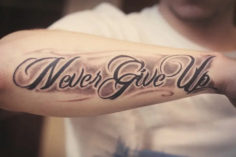 Never give up lettering tattoo on the inner forearm